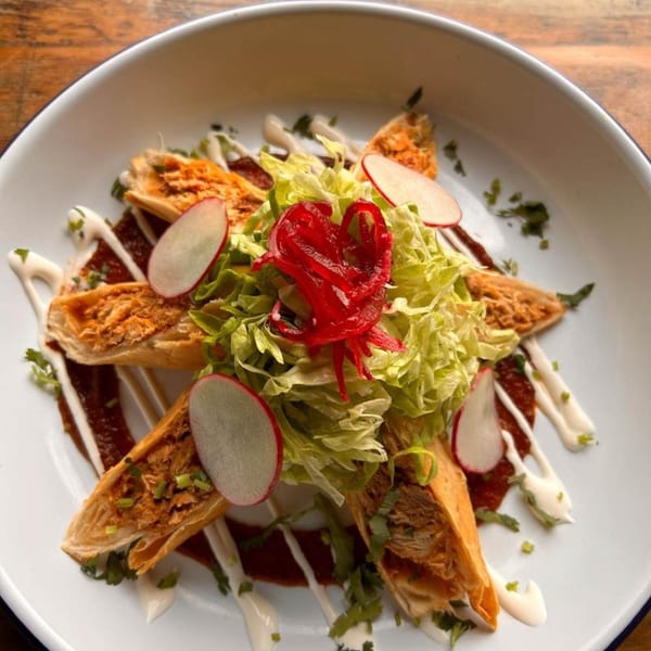 Vaqueros Mexican Restaurant's taquitos with lettuce, radishes, red onions, and crema on a white plate.