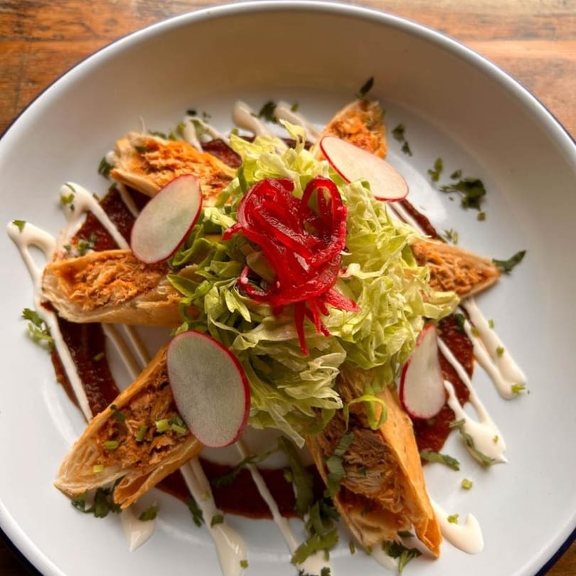 Vaqueros Mexican Restaurant's taquitos with lettuce, radishes, red onions, and crema on a white plate.