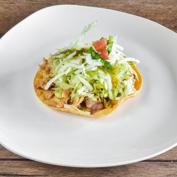 A single Vaqueros Mexican Restaurant tostada, topped with shredded lettuce, salsa verde, and diced tomatoes.