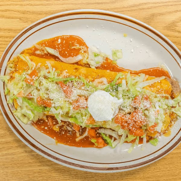 Platter of Vaqueros Mexican Restaurant's enchiladas topped with red sauce, lettuce, tomatoes, cheese, and sour cream.