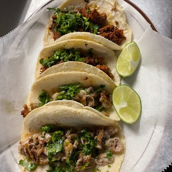 Four Vaqueros Mexican Restaurant tacos with meat and cilantro, served with two lime wedges on white paper.