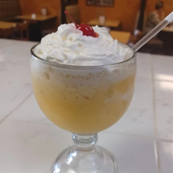 A frozen pineapple drink topped with whipped cream and a cherry, with a straw, at Vaqueros Mexican Restaurant.