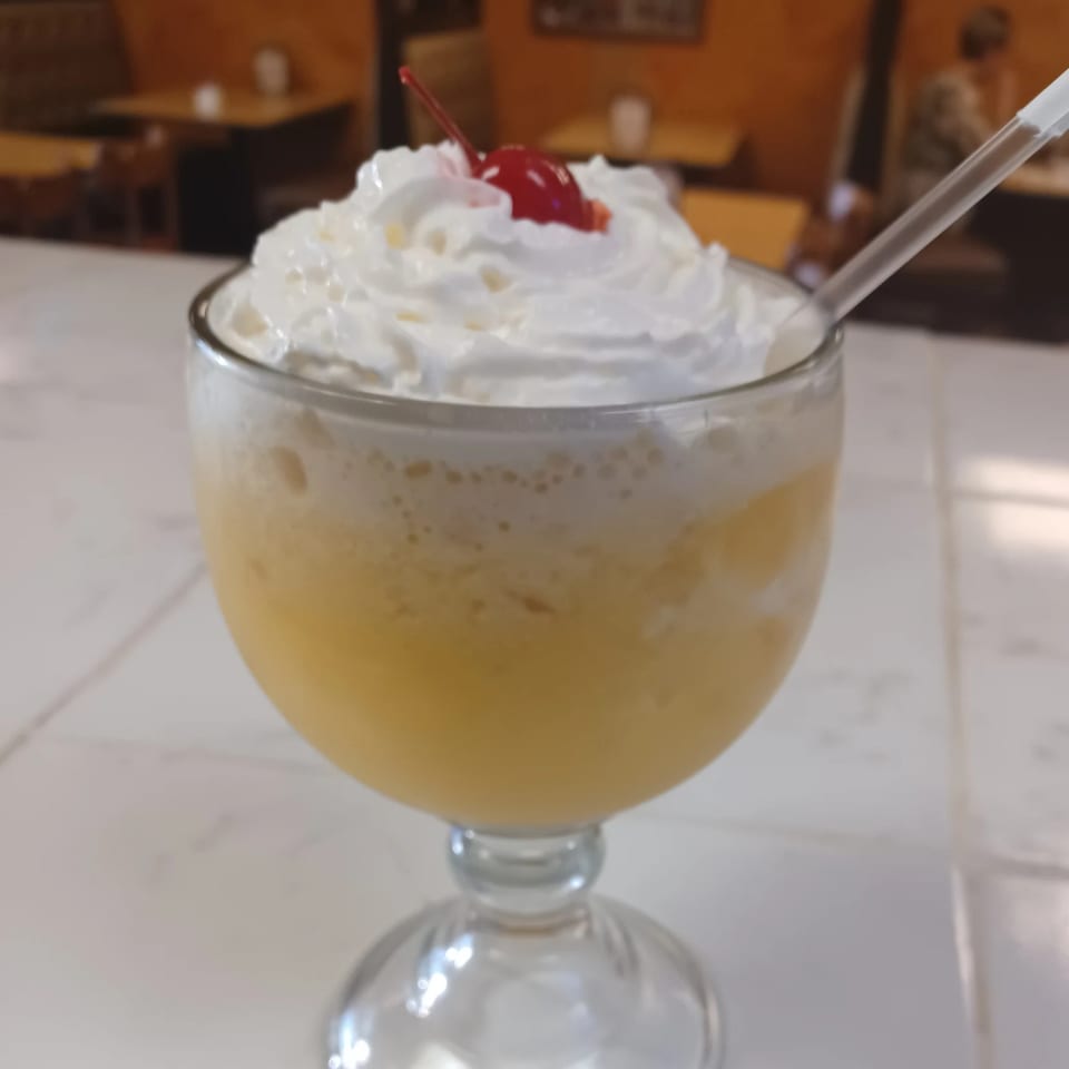 A frozen pineapple drink topped with whipped cream and a cherry, with a straw, at Vaqueros Mexican Restaurant.