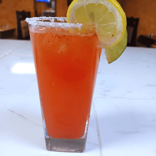A vibrant red drink in a tall glass, garnished with a lemon and lime slice, and a salted rim.