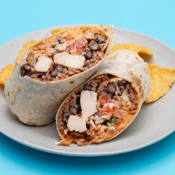 Two halves of a chicken burrito, filled with rice, black beans, and tomatoes, on a plate with tortilla chips.