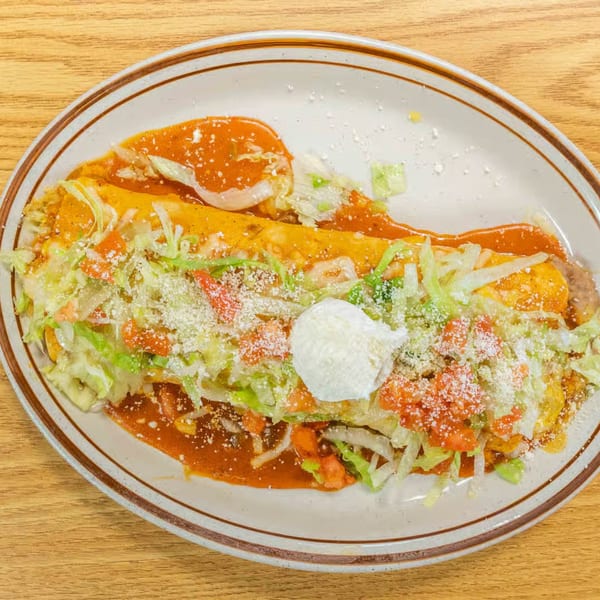 Two Vaqueros Mexican Restaurant enchiladas covered in red sauce, lettuce, tomatoes, cheese, and sour cream.